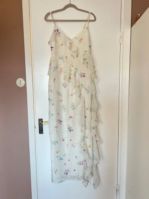 Vit långklänning med volanger och blommor - Klänning, användes vid bröllop en gång efter det aldrig använd. Strl 36/s 