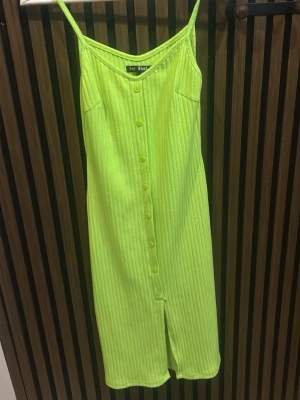 Neongul ribbad klänning Bay Watch - Snygg neongul ribbad klänning från Bay Watch med smala axelband och knappar framtill. Klänningen har en slits nedtill och är perfekt för sommarens varma dagar. Enkel och trendig design som sticker ut.