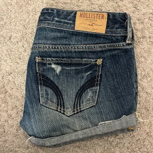 Jeansshorts från Hollister med slitningar - Snygga blå jeansshorts från Hollister med slitna detaljer. Klassisk femficksmodell med dubbla knappar framtill och broderad logga på fickan. Perfekta för en avslappnad stil under varma dagar. Skriv innan köp!!❤️