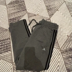 Grå Adidas mjukisbyxor Formotion L - Grå mjukisbyxor från Adidas med Formotion-detalj och svarta ränder längs sidorna. Byxorna har elastisk midja med snörning och dragkedjeficka bak. Perfekta för chill eller träning, riktigt sköna och stilrena.