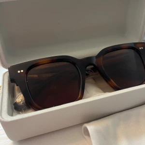 Bruna fyrkantiga solglasögon från CHIMI - Snygga solglasögon från CHIMI med brunmelerad båge i fyrkantig modell. Glasen är mörkbruna och bågen är tillverkad i syntetmaterial. Perfekt accessoar för att lyfta din stil och skydda ögonen mot solen. Kommer med originalfodral och putsduk.