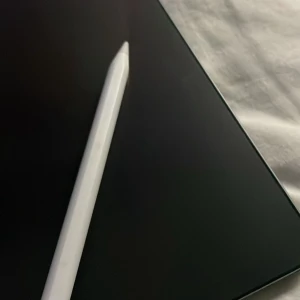 Apple iPad med Apple Pencil - Snygg Apple iPad i mörkgrått med tillhörande Apple Pencil. Plattan ser ut att vara i mycket gott skick utan synliga repor eller skador. Perfekt för studier, kreativt arbete eller underhållning. Apple-loggan och smart connector syns tydligt på baksidan.