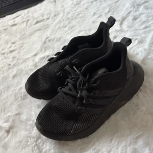 Svarta Adidas sneakers strl 36 - Säljer ett par helsvarta Adidas sneakers i storlek 36. Skorna har en sportig look med mesh-ovandel, platt sula och klassiska tre ränder på sidan. De har snörning och är tillverkade i syntetmaterial som andas. Perfekta för dig som gillar stilrena och bekväma sneakers.