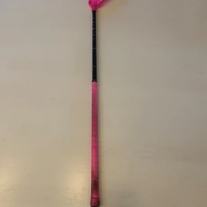 Salming Carbon Pro Innebandyklubba - Salming Carbon Pro innebandyklubba i svart och rosa. Lättviktsklubba med kolfiberskaft och greppvänligt rosa handtag. Bladet är i toppskick och klubban visar minimalt slitage. Perfekt för både träning och match. 96 cm lång och left.