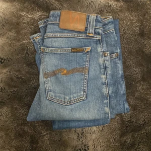 Nudie Jeans - Säljer ett par klassiska blå jeans från nudie jeans. Jeansen har snygga kontrastsömmar, fem fickor och Nudie-logga på bakfickan. Perfekta för dig som gillar en stilren look. Storleken är 27/34 och passar dig som är ungefär 160-168 beror på hur du vill passformen ska vara! Kom med bud och frågor!