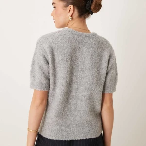 Grå kofta med pärlknappar - Mysig grå kofta i fluffigt stickat material med korta ärmar och rund hals. Stängs med pärlknappar framtill och har en enkel, stilren look. Perfekt för lager-på-lager och passar till både jeans och kjol.