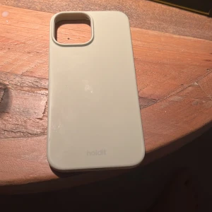 Holdit mobilskal för iPhone - Stilrent beige mobilskal från Holdit, anpassat för iPhone med stor kameramodul. Skalet är i gott skick med endast mindre spår av användning. Perfekt för dig som vill skydda din mobil med en snygg och diskret design.