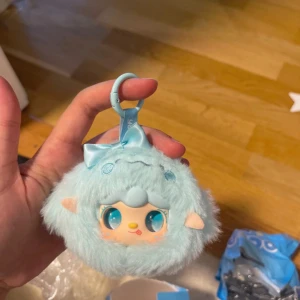 Ocean Baby fluffig blå nyckelring - Supersöt liten fluffig väska från Ocean Baby i ljusblått med ett gulligt ansikte och öron. Väskan har en rund form, mjuk pälsliknande yta och en praktisk karbinhake för att fästa på ryggsäck eller nycklar. Perfekt som accessoar eller nyckelringsväska.