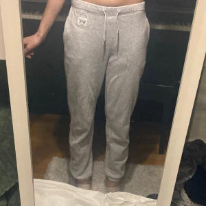 Grå mjukisbyxor från H&M med snören - Grå mjukisbyxor från H&M i storlek 152. Byxorna har resår i midjan med snörning och en liten NYC-patch framtill. De är raka i modellen och i bomull.