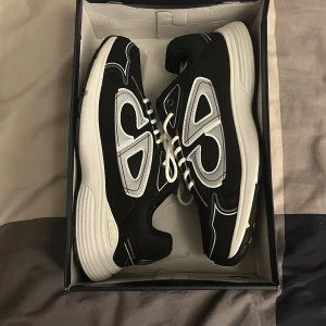 Svarta och vita B30 sneakers - Säljer ett par helt nya B30 sneakers i svart och vitt med reflekterande detaljer och tydlig logga på sidan och sulan. Skorna har snörning, platt sula och rund tå. Ovandelen är i mesh och syntet med coola grafiska inslag. Perfekt för dig som gillar exklusiva sneakers med statement. Skriv för mer bilder osv…