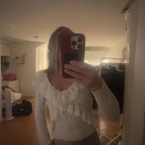 Vit stickad blus från Zara med spetsvolang - Superfin vit stickad blus med lång ärm och bred v-ringning. Blusen har detaljerad spetsvolang runt halsen och framtill. Materialet är stickat med snyggt mönster. Perfekt för dig som gillar söta detaljer!