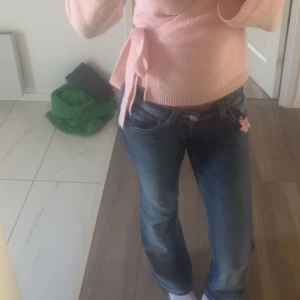 Blå jeans med broderad ficka - Säljer ett par blå jeans med snygg broderad bakficka och dekorativa paljetter. Jeansen har låg midja och en rak passform. Materialet är klassisk denim och de har en liten rosa blomdetalj vid fickan framtill.