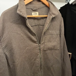 Beige overshirt från East West - Snygg beige overshirt från East West med dragkedja framtill och en bröstficka. Skjortan har en avslappnad passform och är tillverkad i ett strukturerat bomullstyg. Perfekt att slänga över en t-shirt för en chill look.