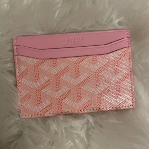 Rosa Goy4rd plånbok med mönster - Superfin plånbok från Goy4rd i rosa med deras ikoniska mönster i ljusrosa och korall. Slimmad design med flera kortfack och detaljer i skinn. Perfekt att ha i fickan eller en mindre väska. Kommer med originalbox och dustbag.