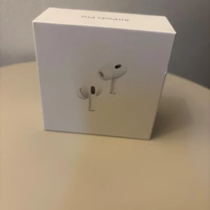 AirPods Pro - Säljer ett par Apple AirPods Pro i originalförpackning. Kartongen ser ut att vara obruten och hörlurarna är troligen oanvända. Aktiv brusreducering, trådlös laddning och hög ljudkvalitet. Liten skavank syns på kartongens kant, annars i mycket fint skick.