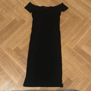 Svart offshoulder långklänning Bershka - Svart långklänning från Bershka med offshoulder-design. Klänningen har en smickrande, figurnära passform och är tillverkad i ett mjukt, stretchigt material. Perfekt för dig som gillar en stilren och enkel look med en twist.
