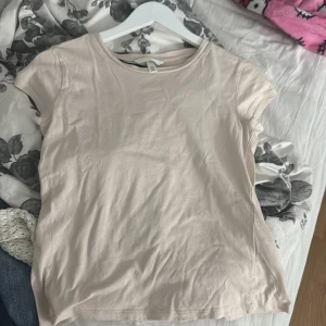 Beige basic t-shirt från H&M - En enkel och stilren beige t-shirt från H&M i storlek S. T-shirten har rund halsringning och korta ärmar, tillverkad i mjuk bomull. Perfekt till jeans eller kjol för en clean look. Den har en liten fläck men syns knappt