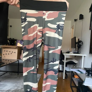 Camo leggings med hög midja - Säljer ett par tighta leggings med camouflagemönster i grönt, rosa, svart och vitt. De har hög midja med bred svart linning och snygg rynkdetalj bak. Perfekta för dig som vill sticka ut på gymmet eller i vardagen.