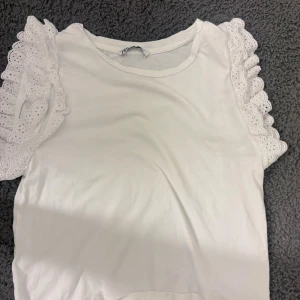 Vit blus med spetsvolang från Zara - Säljer en vit blus från Zara i storlek S. Toppen har rund hals och korta ärmar 