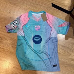 Barça Lamine Yamal #10 Nike fotbollströja - Säljer en Barcelona fotbollströja med Lamine Yamal och nummer 10 på ryggen. Tröjan har coola färgskiftningar i blått, rosa och turkos, med Champions League-märke på ärmen och Spotify-logga på bröstet. Tillverkad i lätt polyester, perfekt för match eller träning.