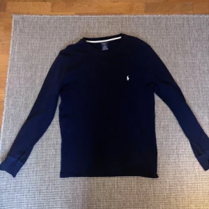Mörkblå långärmad tröja Polo Ralph Lauren - Mörkblå långärmad tröja från Polo Ralph Lauren i 100% bomull. Klassisk passform med rund hals och diskret broderad logga på bröstet. Perfekt för en stilren och enkel look.