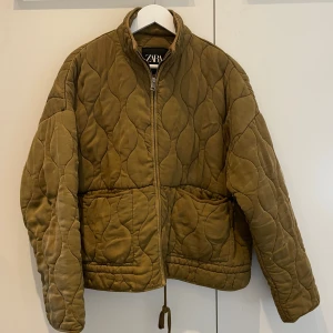 Quiltad jacka från Zara - Populär grön/khaki Quiltad jacka från Zara Jackan har dragkedja framtill, två stora fickor och snörning nedtill. nypris omkring 700. inga defekter utöver lite nopror, därav priset! väldigt varm perfekt till senhöst/vinter/vår