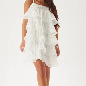 Vit volangklänning till Studenten - Superfin vit kortklänning med flera lager volanger och tunna axelband. Klänningen har plisserat tyg som ger en luftig känsla. Endast använd vid ett tillfälle. Obs! Klänningen är uppsyd cirka 5cm då den var för lång på mig som är cirka 164. Inga defekter, som ny! Pris kan diskuteras 🫶🏻köpt för 1200kr