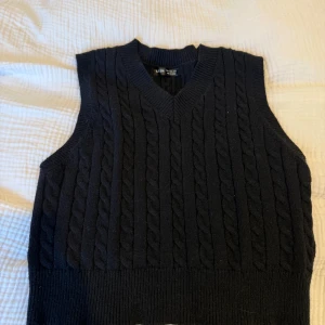 Svart stickad väst - Svart kabelstickad väst från SHEIN med v-ringning och ribbade kanter. Klassisk och enkel design som är lätt att styla över en skjorta eller t-shirt. Perfekt för lager-på-lager och ger en snygg preppy vibe.