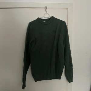 Mörkgrön stickad tröja från Dobber - En enkel och stilren mörkgrön stickad tröja från Dobber med rund halsringning och ribbade muddar vid ärmslut och nederkant. Perfekt med jeans. Passar både S och M