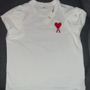 Vit Ami T-shirt - Säljer en stilren vit ami T-shirt, T-shirten är knappast använd, väldigt skön och stilig.  Storlek S men passar M