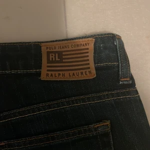 Bootcut jeans från Ralph Lauren - Snygga mörkblå bootcut jeans från Ralph Lauren Polo Jeans Company. Modellen är low rise med klassisk femficksdesign, stretchigt jeanstyg och dragkedjegylf. Perfekta för dig som gillar en tidlös och avslappnad look.