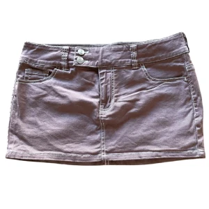 Brun mini jeans kjol  med fickor och knappar - Snygg brun kortkjol med två framfickor, två bakfickor och dubbla knappar i midjan. Kjolen har synliga vita sömmar och bälteshällor, vilket ger en cool och avslappnad vibe. Perfekt för dig som gillar enkel och stilren design.