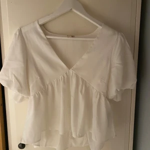 Vit blus från Nelly - Supersöt vit blus från Nelly med v-ringning och puffiga korta ärmar💕endast använd en gång och är i nyskick! Super skönt material och verkligen så gullig! Säljer då den tyvärr är för liten för mig ⚡️