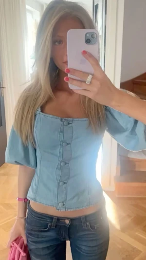 Ljusblå topp med puffärm - Säljer en ljusblå topp med puffiga korta ärmar och snygga knappar framtill. Toppen har en fyrkantig urringning och är croppad i modellen. Materialet är denimliknande och ger en cool vibe till outfiten.