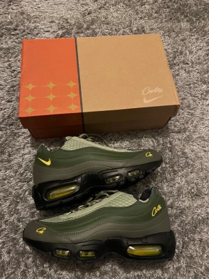 Nike Air Max 95 x Corteiz olivgröna sneakers - Nike Air Max 95 x Corteiz sneakers i olivgrönt och mörkgrönt med svarta och gula detaljer. Skorna har snörning, synliga Air Max-bubblor med gul insida och camo-mönstrat foder. Materialmix av syntet och textil med broderad Corteiz-logga på sidan och tån.