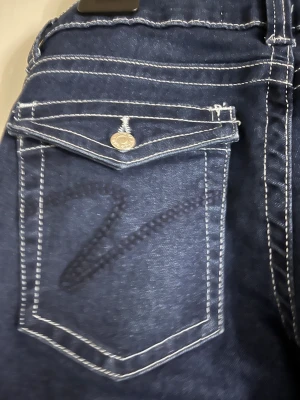 Bootcut jeans från Din Vintage Shop XS - Mörkblå bootcut jeans med kontrasterande vita sömmar och snygga fickdetaljer med lock och knapp bak. Klassisk femficksmodell i stretchig denim som sitter skönt och ger en cool siluett. Perfekt för dig som gillar retrovibbar och markerade detaljer.