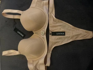 Beige Lounge mesh bh med trosa  - Säljer en beige mesh bh 85b från Lounge med stringtrosa. Bh har slät yta, lätt vadderade kupor och snygga metallspännen framtill. Materialet är mjukt och stretchigt, perfekt för en chill look.