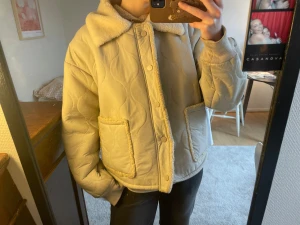 Meotine jacka, exad Teddyjacka beige med krage -  suite en mysig beige teddy pipeline med quiltad design och fluffig krage. Jackan har stora fickor med teddy-detaljer, tryckknappar framtill och ribbade muddar vid ärmsluten. Perfekt för dig som gillar oversized och chill stil.