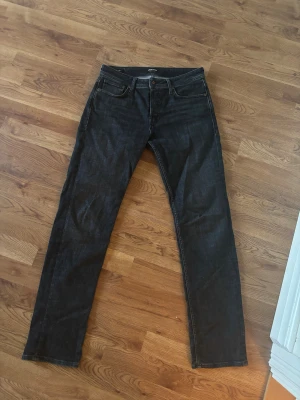 Svarta jeans från Jack & Jones - Säljer ett par svarta jeans från Jack & Jones med klassisk femficksdesign och snygga kontrastsömmar. Jeansen har rak passform och är tillverkade i slitstarkt denimtyg. Perfekta för dig som gillar en clean och tidlös look. De är helt nya och är i storlek 30w 32L