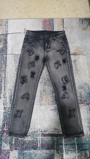 Svarta jeans med broderade bokstäver - Unika svarta jeans med broderade bokstäver och grova slitningar framtill. Jeansen har klassisk femficksdesign och raka ben. Materialet är robust denim och färgen är mörkgrå/svart med tvättad look. Perfekt för dig som vill sticka ut med en cool streetstil.