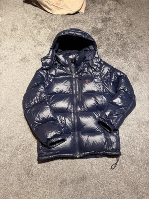 Mörkblå pufferjacka från Polo Ralph Lauren - Säljer min mörkblåa vinter jacka från Polo Ralph Lauren, skicket är som nytt. Digitalt kvitto finns på sista bilden, den är givetvis äkta och köpt från Ralph Laurens officiella hemsida. Jackan är använd endast en vinter och har inga defekter som till exempel skador mm. Ställ gärna frågor om det undras något.