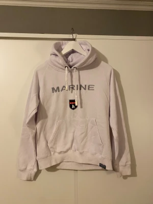 Vit hoodie från Marine  - Vit hoodie från Marine Scandinavian Sportswear. Tröjan har huva med snörning, stor magficka och ribbade muddar. Har en liten fläck över fickan
