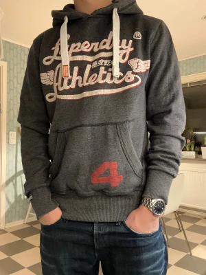 Superdry Atl hoodie - Detta är en riktigt go hoodie som är snygg till allt! Älskar denna layouten och trycket😮‍💨Trycket är sprucket vilket ger den en riktigt najs vintage look🤩! Storlek S med en skön passform. En väldigt liten fläck som syns på sista bilden, knappast synlig när man har på sig den. Skicka gärna frågor!