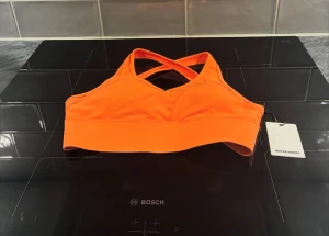 Orange sportig linnetopp från Better Bodies - Snygg och sportig orange linnetopp från Better Bodies i strl xs kostar 499 kr ord pris, med korsade axelband i ryggen. Toppen är tillverkad i mjukt och stretchigt syntetmaterial som sitter skönt under träningen. Perfekt för gymmet eller andra aktiva dagar. Taggen sitter kvar.