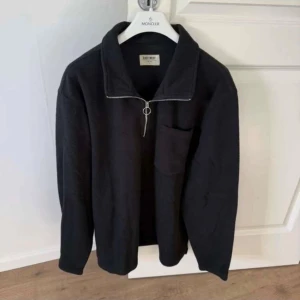 Svart fleece-tröja från East West L - Svart fleece-tröja från East West i storlek L. Tröjan har en half zip-dragkedja med metallring, hög krage och en bröstficka. Perfekt för kyliga dagar och har en clean, enkel look som funkar till jeans eller mjukis.