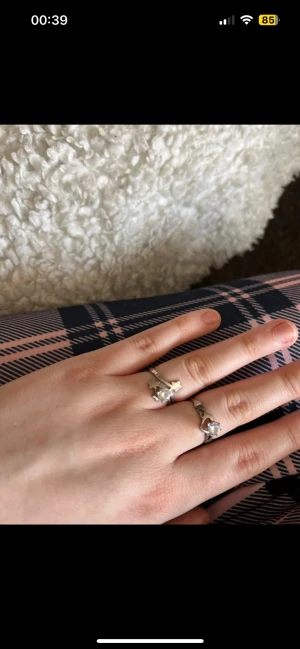 Två silverringar med stenar - Säljer två snygga silverfärgade ringar med glittrande stenar. Båda ringarna har detaljerade infattningar och en klassisk rund form. Perfekt för dig som gillar stilrena accessoarer med lite extra bling.