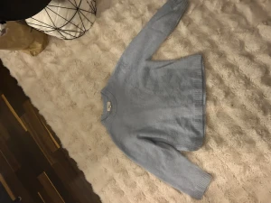 Ljusblå stickad tröja Gina Tricot - Mysig ljusblå stickad tröja från Gina Tricot i ullblandning. Tröjan har rund hals, ribbade muddar och lång ärm. Perfekt för att hålla värmen under kyliga dagar och passar dig som gillar enkel och stilren design.