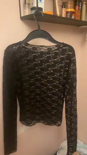 Säljer en svart långärmad blus i genombruten spets med blommigt mönster. Toppen har rund hals och är figurnära i modellen, perfekt för dig som gillar en elegant och lite edgy stil. Spetsen ger en snygg transparent effekt och blommiga detaljer gör den extra fin.