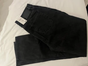 Svarta Seattle jeans från 157, W31 L34 - Svarta jeans från 157, modellen Seattle med hög midja och relaxed fit. Klassisk femficksdesign, raka ben och snygga detaljer i silver. Perfekt för dig som gillar en enkel och stilren look. Materialet är slitstark denim i bomull.