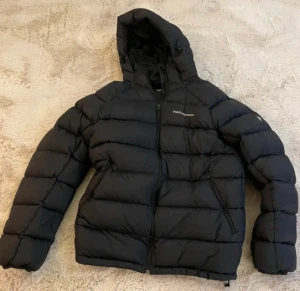 Svart Peak Performance dunjacka - Svart dunjacka från Peak Performance (använd 1-2ggr) med huva och dragkedja. Perfekt för kalla dagar och har en clean, sportig look. Broderad logga på bröstet.      Hör av er vid fler frågor!